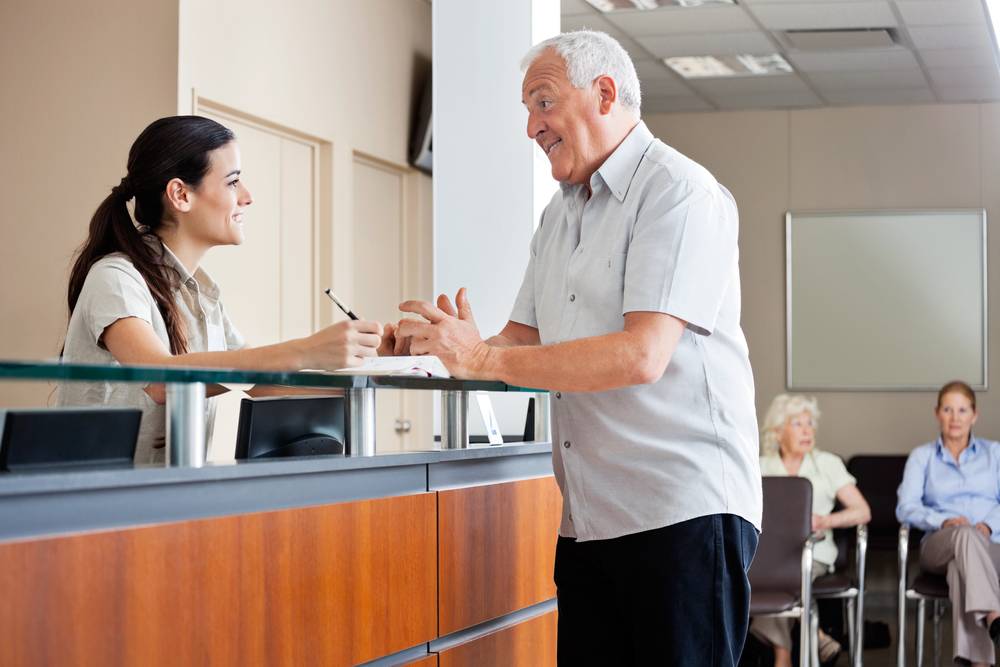 Senior,Man,Communicating,With,Female,Receptionist,While,Women,Sitting,In